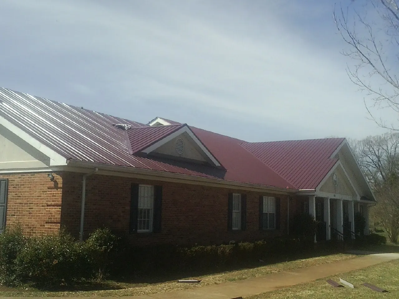 Red metal roof with gabled entries on a long brick building, from a Hail Damage Roof Repair job in Porter Corners