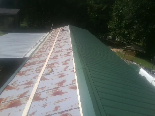 Old rusted panels beside newly installed green metal roofing — Wind Damage Roof Repair by Roofing Brothers in Porter Corners