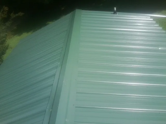 New green metal panels meeting at the ridge of a roof — Flat Roof Repair work by our crew in Porter Corners