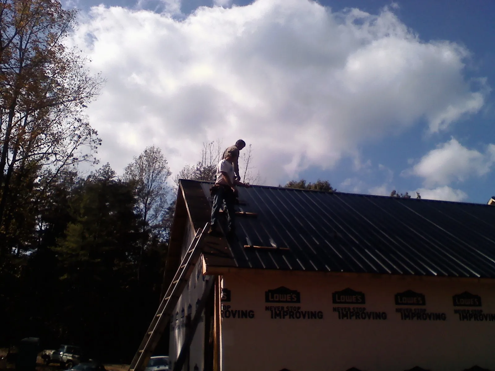 Roofer fastening dark metal panels high against a cloudy sky, from a Roof Inspection job in Porter Corners
