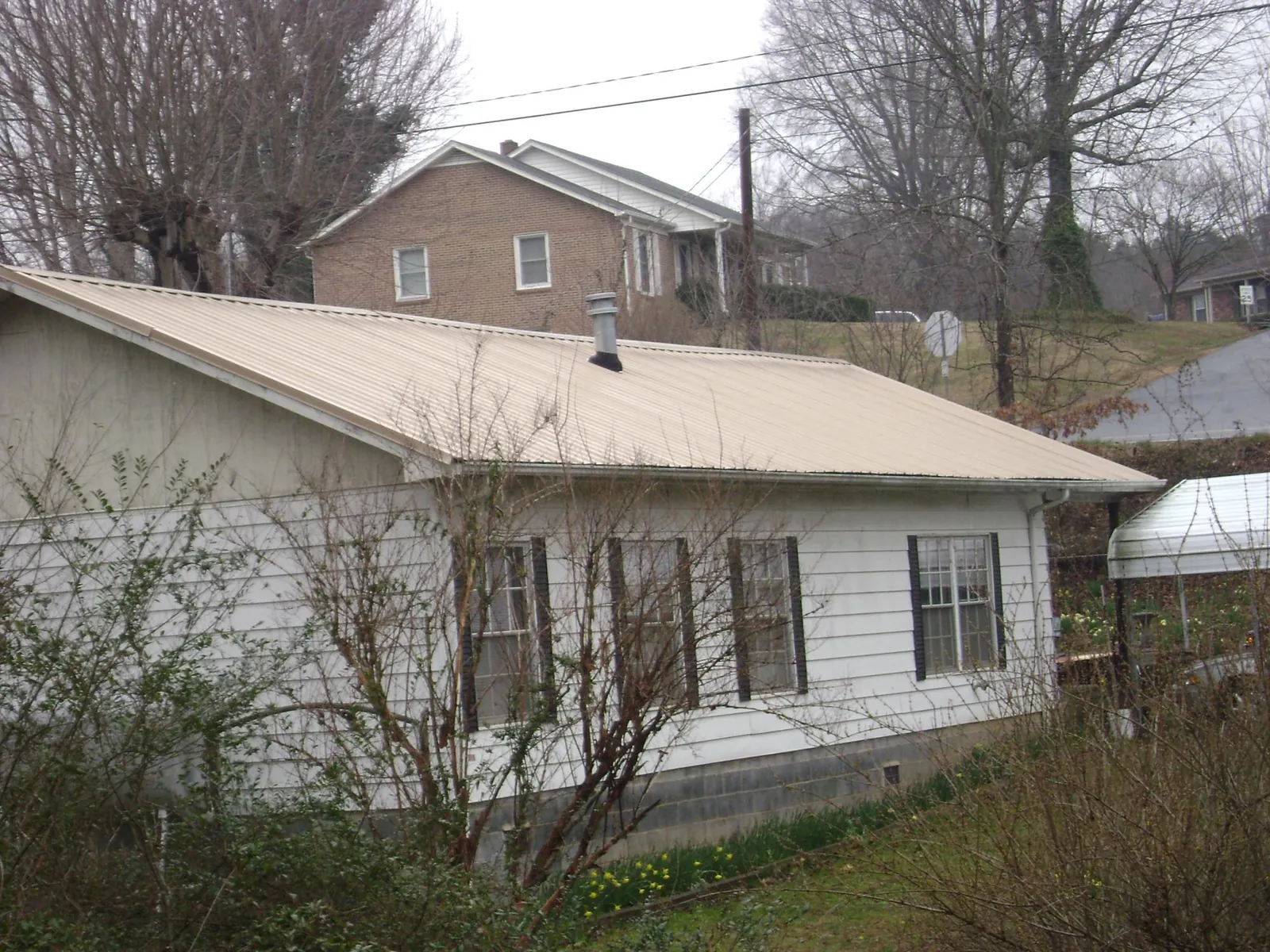 Tan metal roof on a white sided house set into a hillside — Commercial Roofing by Roofing Brothers in Porter Corners