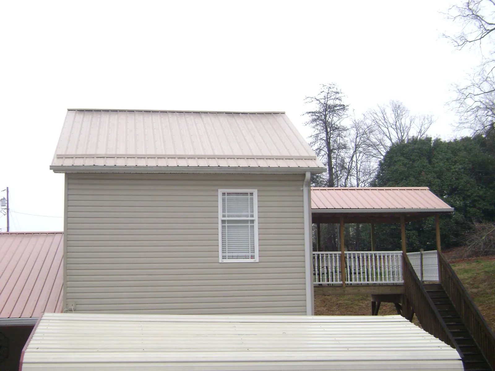 Tan metal roofs on a two story addition and attached porch, from a Roof Replacement job in Porter Corners